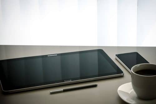Présentation d'une tablette posé sur une table avec un stylet un smartphone et une tasse de café